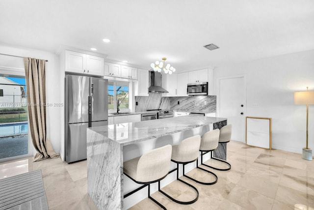 kitchen with visible vents, appliances with stainless steel finishes, wall chimney range hood, white cabinetry, and a sink