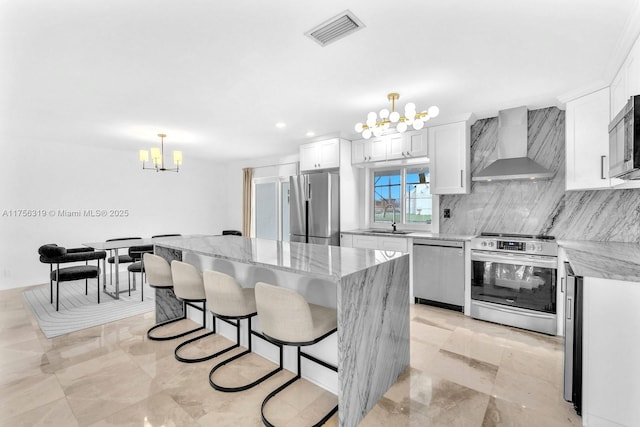 kitchen with visible vents, wall chimney exhaust hood, light stone countertops, stainless steel appliances, and a chandelier