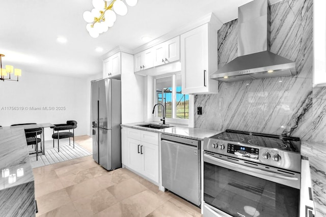 kitchen with light stone counters, a notable chandelier, appliances with stainless steel finishes, a sink, and wall chimney exhaust hood