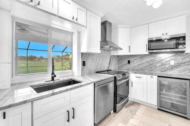 kitchen featuring stainless steel appliances, white cabinets, a sink, wall chimney range hood, and beverage cooler