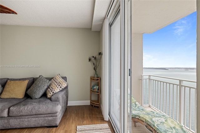 living room featuring a textured ceiling, a water view, wood finished floors, and baseboards