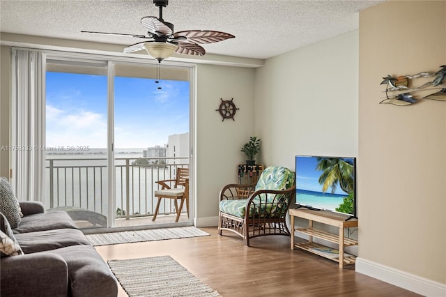 living room with baseboards, a textured ceiling, a ceiling fan, and wood finished floors