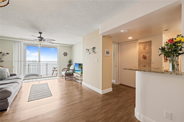 living area featuring ceiling fan, a textured ceiling, baseboards, and wood finished floors