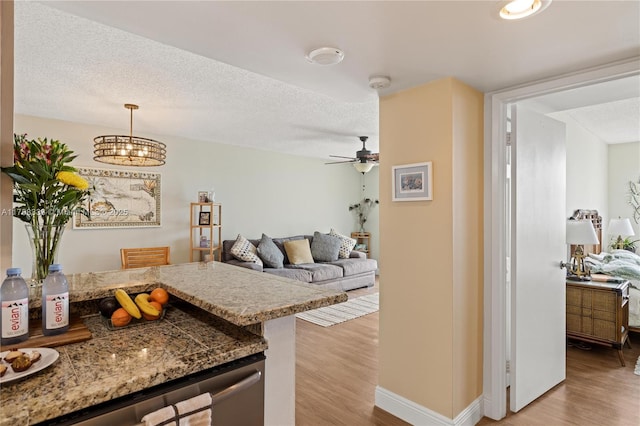 kitchen with a textured ceiling, ceiling fan, baseboards, light wood finished floors, and pendant lighting