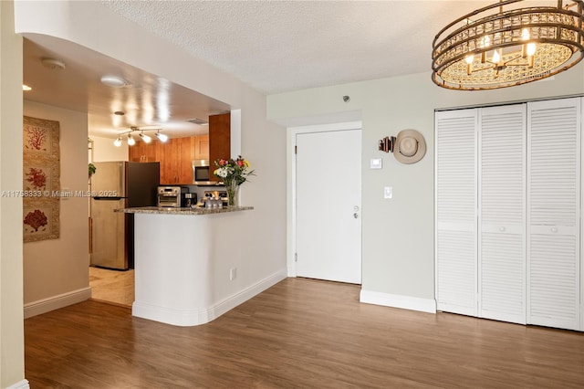 kitchen with a textured ceiling, baseboards, stainless steel appliances, and wood finished floors