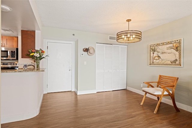 sitting room with visible vents, a textured ceiling, baseboards, and wood finished floors