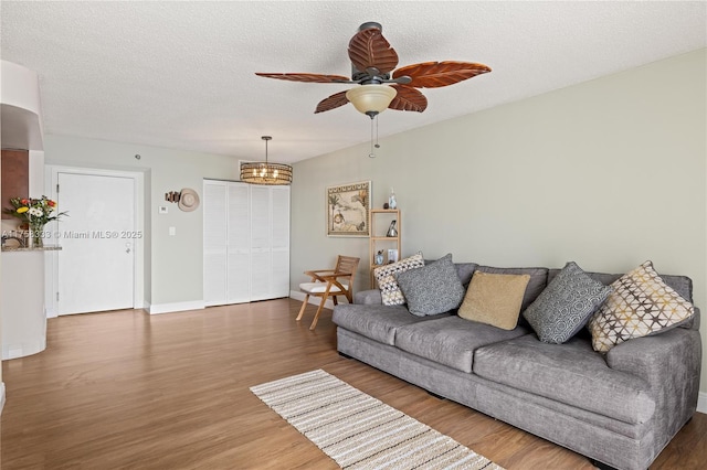 living area with ceiling fan, a textured ceiling, baseboards, and wood finished floors