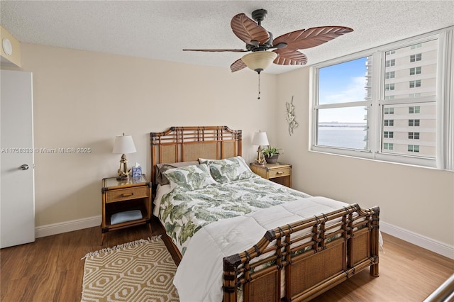 bedroom featuring a ceiling fan, a textured ceiling, baseboards, and wood finished floors