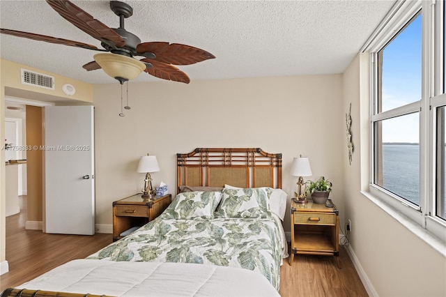 bedroom featuring a textured ceiling, wood finished floors, visible vents, and baseboards