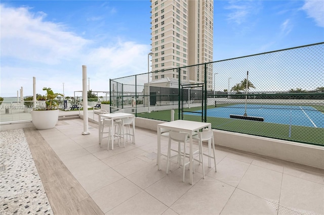 view of patio / terrace featuring a tennis court and fence