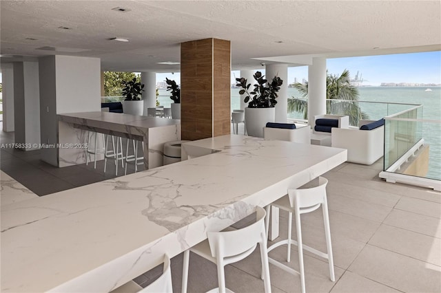 kitchen featuring a textured ceiling, stone countertops, tile patterned flooring, a breakfast bar, and a water view