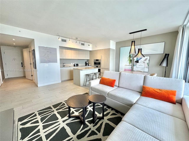 living area featuring baseboards, light wood-style flooring, visible vents, and track lighting