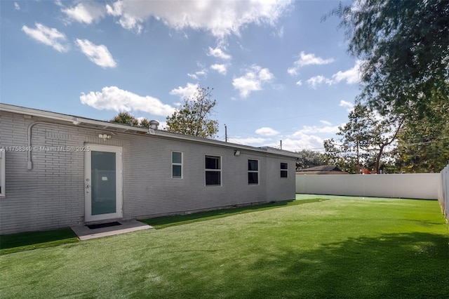 rear view of property featuring a yard, brick siding, and fence private yard