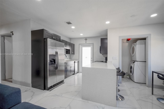 kitchen with recessed lighting, stacked washer / drying machine, marble finish floor, appliances with stainless steel finishes, and light countertops