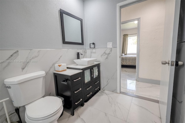 ensuite bathroom featuring connected bathroom, wainscoting, toilet, marble finish floor, and vanity