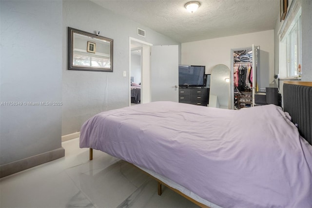 bedroom featuring baseboards, visible vents, a walk in closet, a textured ceiling, and a closet