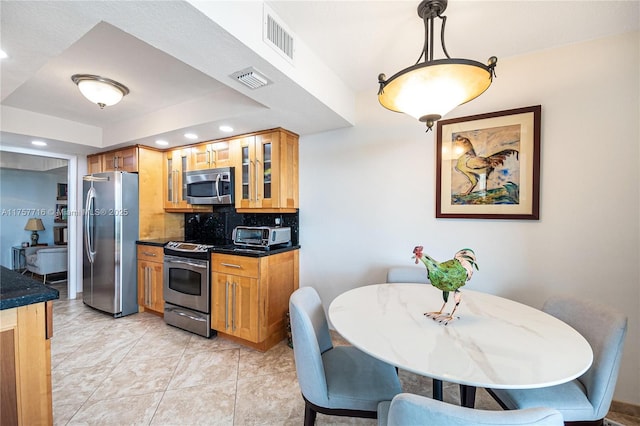 kitchen with stainless steel appliances, dark countertops, visible vents, and decorative backsplash