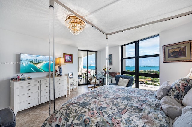 bedroom with a textured ceiling, a water view, access to outside, a wall of windows, and an inviting chandelier