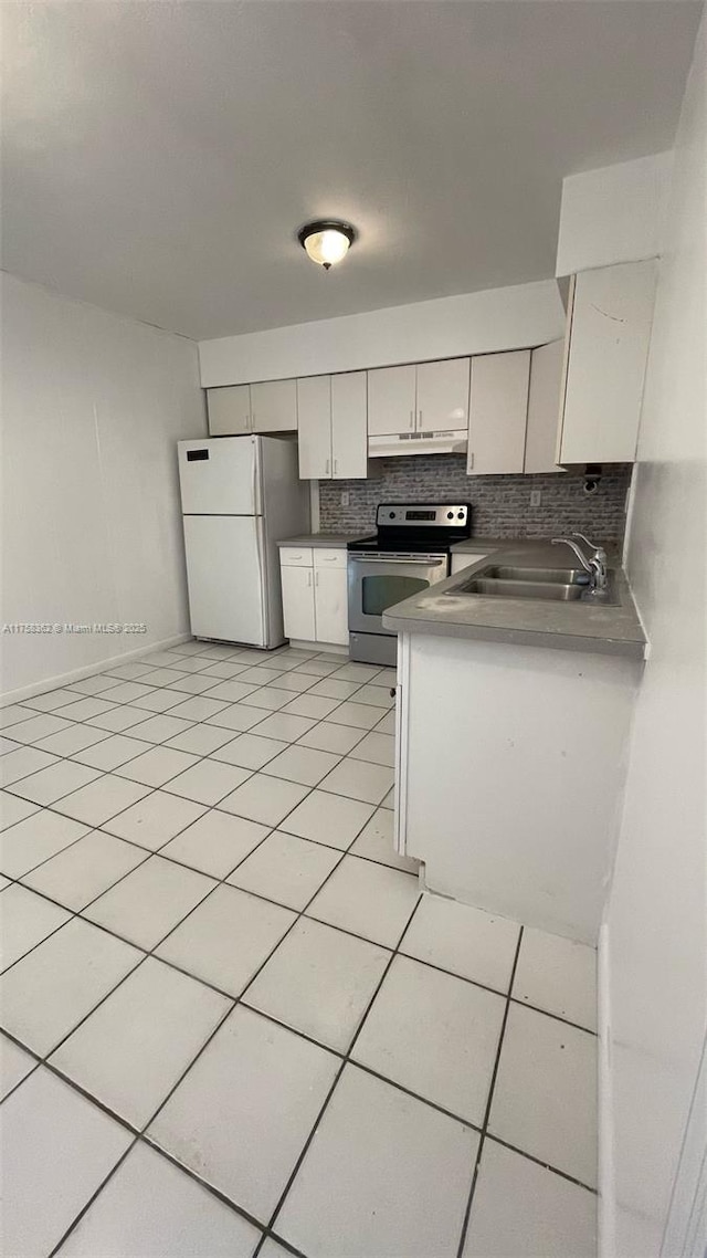 kitchen with light tile patterned floors, electric stove, freestanding refrigerator, under cabinet range hood, and a sink