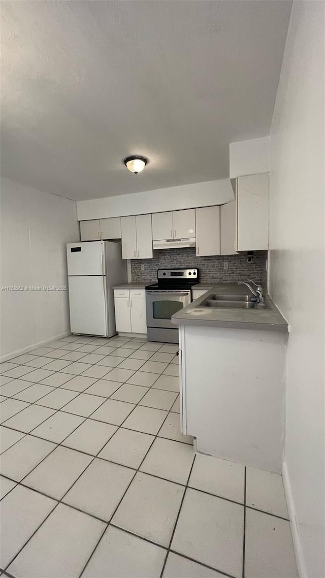 kitchen featuring stainless steel electric range oven, light tile patterned floors, backsplash, freestanding refrigerator, and a sink