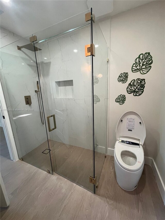 bathroom featuring toilet, wood finished floors, and a marble finish shower