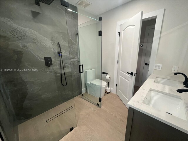 bathroom with toilet, double vanity, a sink, and a marble finish shower