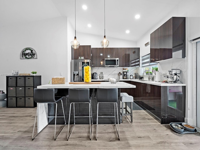 kitchen featuring dark brown cabinets, a breakfast bar area, light countertops, appliances with stainless steel finishes, and modern cabinets