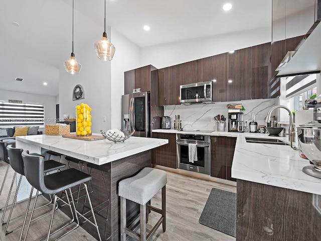 kitchen featuring a sink, dark brown cabinets, appliances with stainless steel finishes, a kitchen bar, and tasteful backsplash