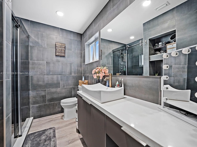 full bathroom with visible vents, toilet, tile walls, a shower stall, and vanity