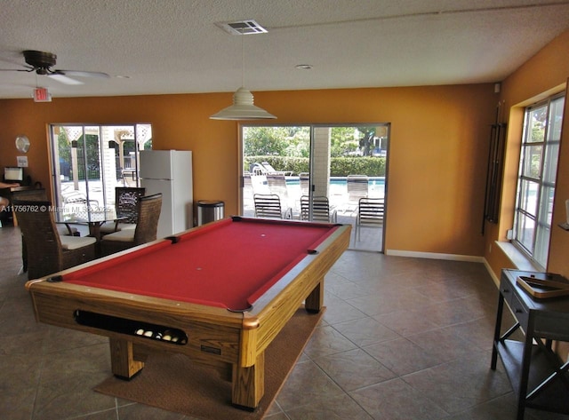 game room featuring a textured ceiling, tile patterned flooring, a ceiling fan, visible vents, and baseboards