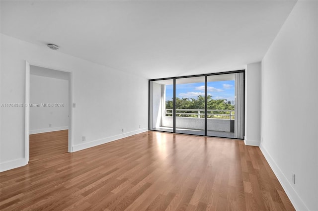 unfurnished room featuring baseboards, a wall of windows, and wood finished floors