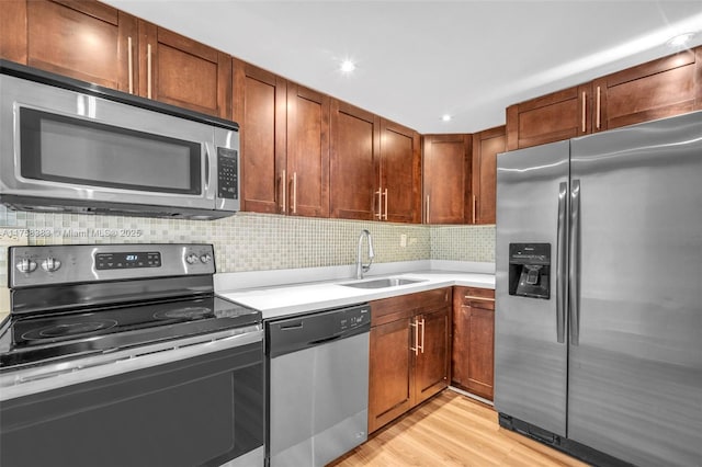 kitchen with light wood-style flooring, stainless steel appliances, a sink, light countertops, and backsplash