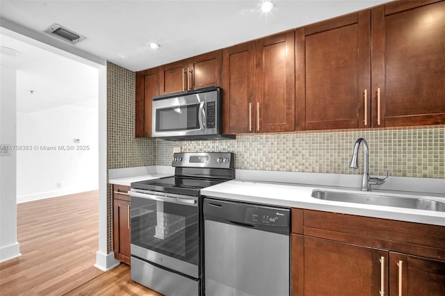 kitchen featuring visible vents, decorative backsplash, stainless steel appliances, light countertops, and a sink