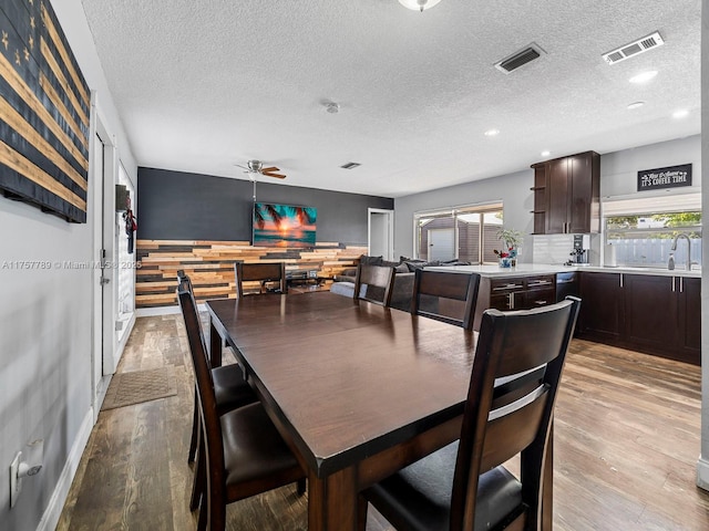 dining area featuring light wood-style floors, visible vents, a textured ceiling, and a ceiling fan