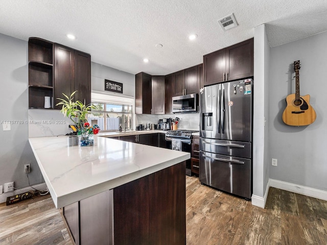 kitchen with stainless steel appliances, visible vents, dark brown cabinets, wood finished floors, and a peninsula