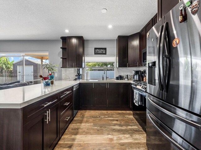 kitchen with a peninsula, dark brown cabinetry, appliances with stainless steel finishes, and wood finished floors