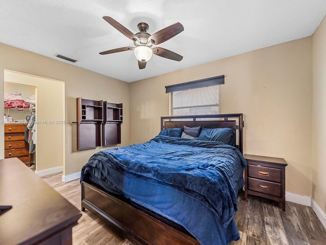 bedroom with ceiling fan, wood finished floors, visible vents, baseboards, and a spacious closet