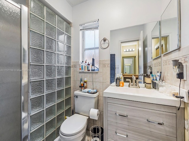 full bathroom featuring wainscoting, toilet, walk in shower, vanity, and tile walls