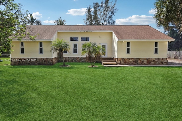 back of property with roof with shingles, a lawn, and fence