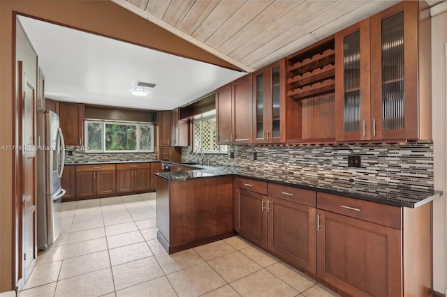 kitchen featuring light tile patterned flooring, vaulted ceiling, backsplash, and freestanding refrigerator