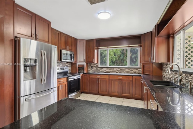 kitchen featuring light tile patterned floors, stainless steel appliances, decorative backsplash, a sink, and dark stone countertops