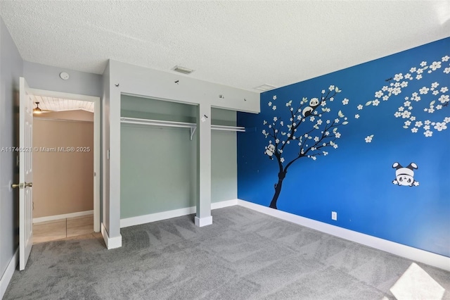 unfurnished bedroom with visible vents, baseboards, a textured ceiling, carpet floors, and multiple closets