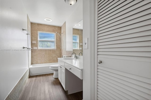 bathroom with toilet, wood finished floors,  shower combination, vanity, and tile walls