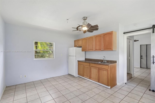 kitchen with dark countertops, a barn door, freestanding refrigerator, ceiling fan, and a sink