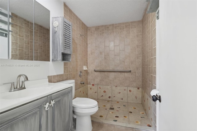 bathroom with a textured ceiling, tile patterned flooring, toilet, vanity, and tiled shower