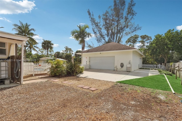 view of side of home featuring a garage, fence, concrete driveway, roof with shingles, and stucco siding