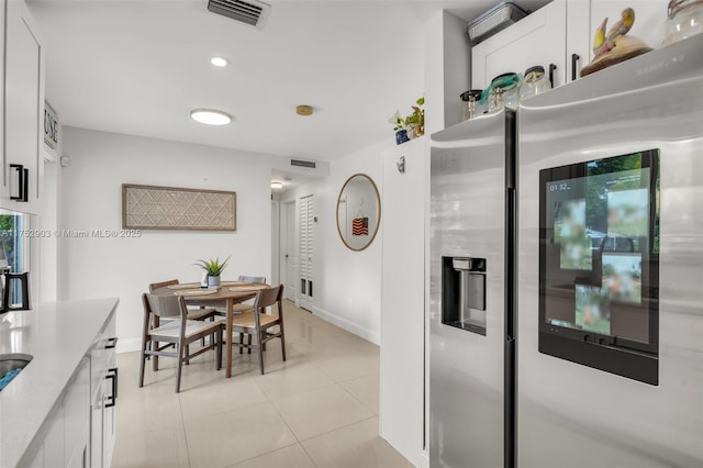 kitchen with light tile patterned flooring, stainless steel refrigerator with ice dispenser, visible vents, and white cabinetry