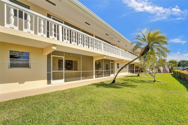 back of property with a balcony, stucco siding, and a yard