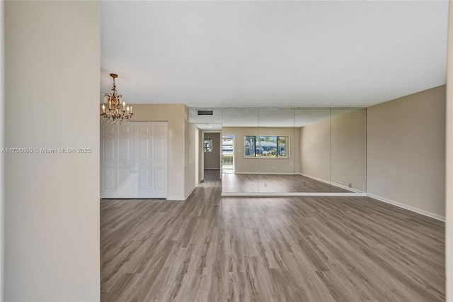 empty room featuring an inviting chandelier, visible vents, baseboards, and wood finished floors