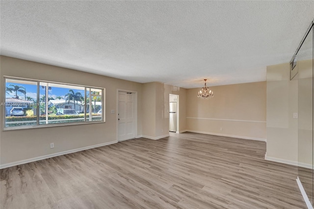 spare room with baseboards, light wood-style floors, a textured ceiling, and an inviting chandelier